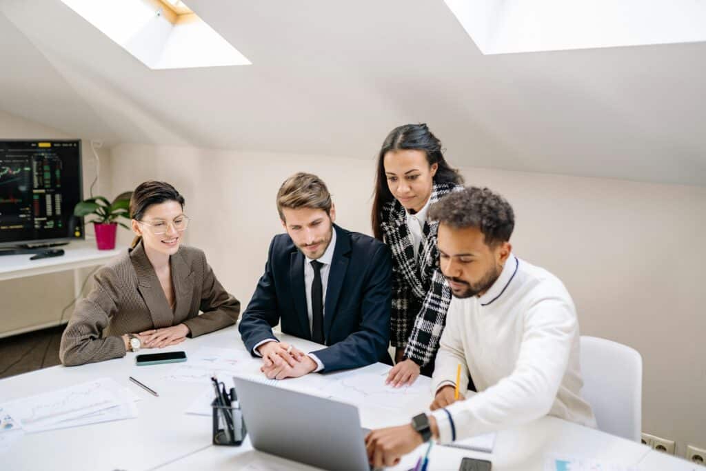 eam of professionals collaborating around a laptop during a business meeting, planning strategies to reduce hire cost and improve recruitment efficiency.